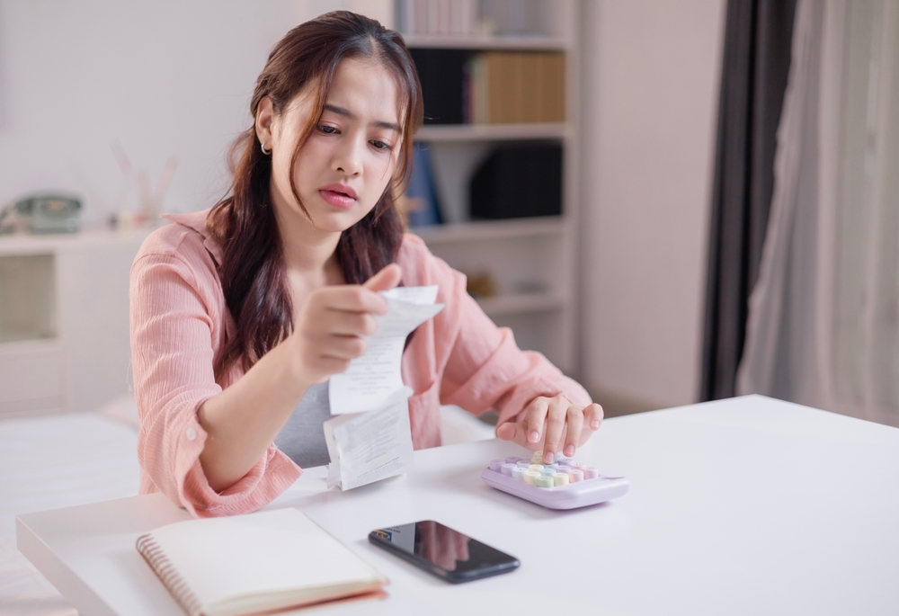 หญิงสาวกำลังพิจารณาฐานเงินเดือนและภาระหนี้จากบิลค่าใช้จ่ายต่าง ๆ ก่อนกู้ซื้อคอนโด